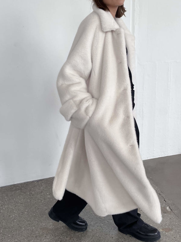 A model wears a cozy, oversized white MEOTINE coat, styled with black pants, showcasing a chic and modern look.