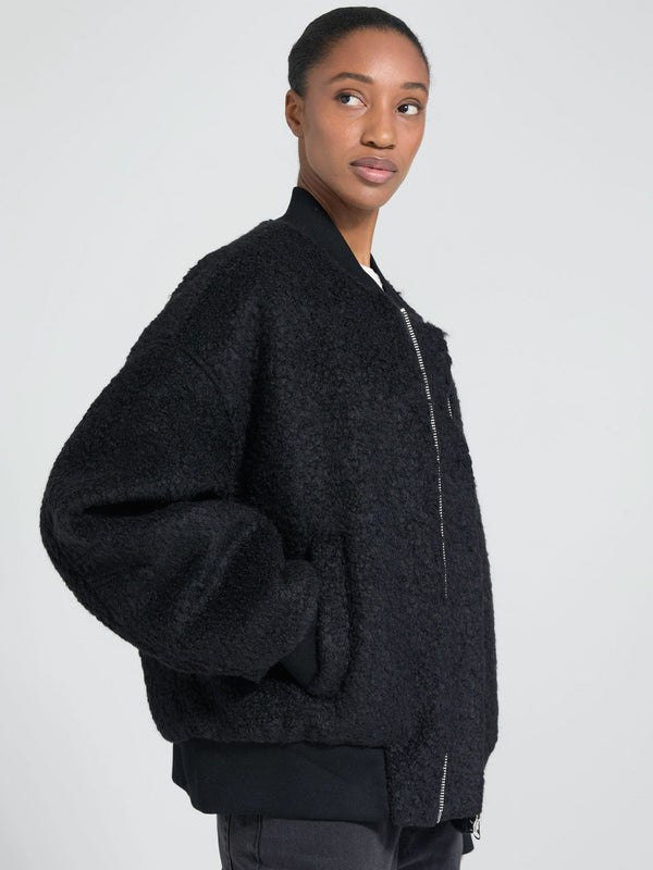 A model showcases a cozy black MEOTINE bomber jacket with a textured finish, featuring a relaxed fit and side pockets.