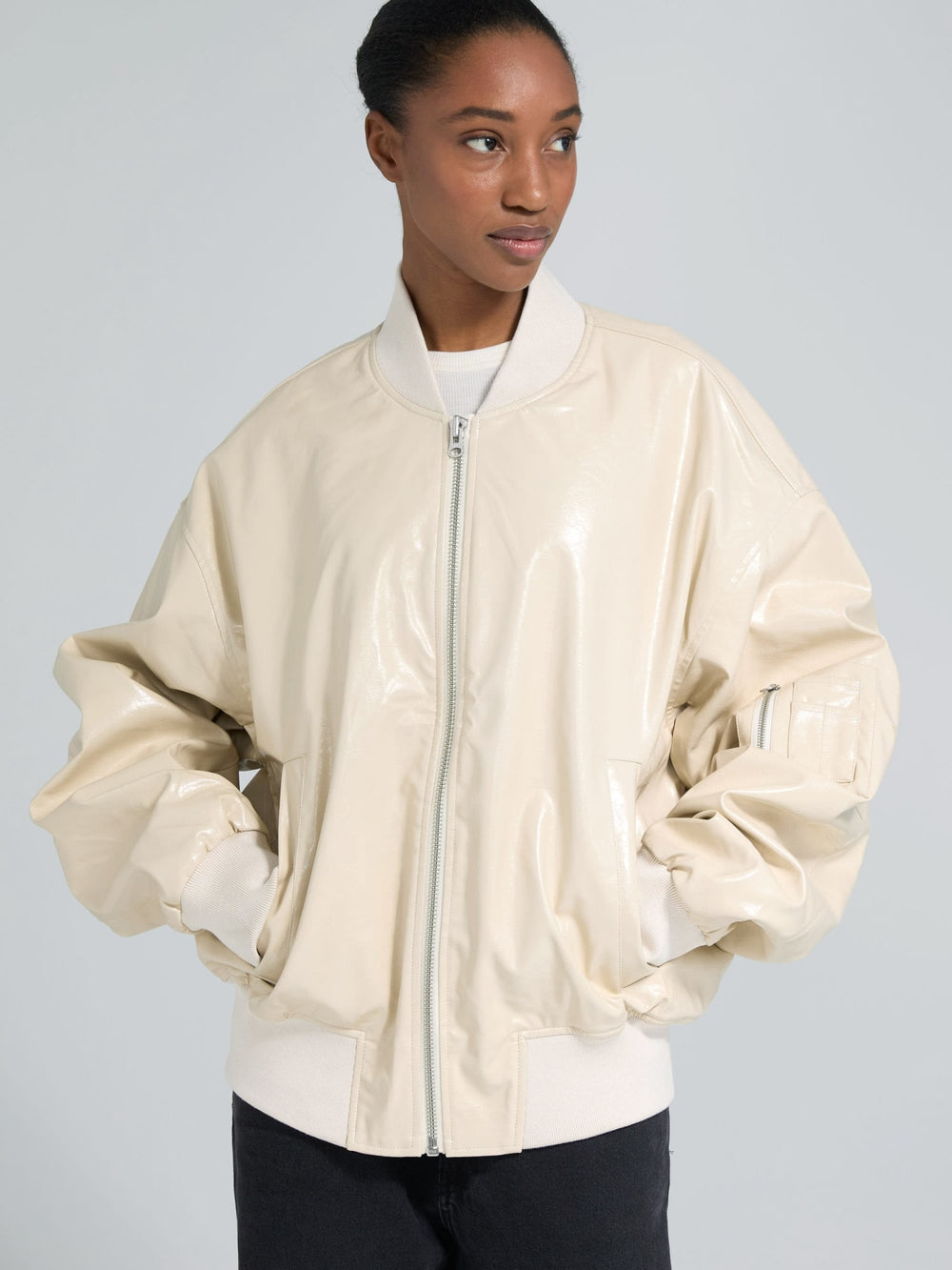 A model wears a glossy beige bomber jacket with oversized sleeves, showcasing a stylish and modern look by MEOTINE.