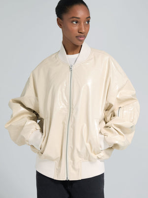 A model wears a glossy beige bomber jacket with oversized sleeves, showcasing a stylish and modern look by MEOTINE.