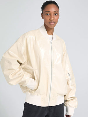 A model showcases a stylish cream-colored bomber jacket with a shiny finish, featuring a zip closure and ribbed cuffs. MEOTINE.