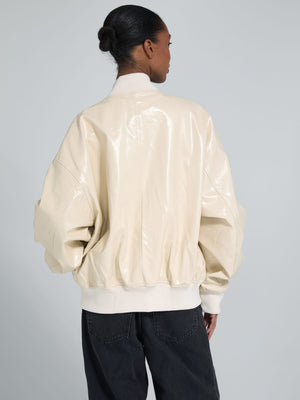 A model showcases a cream-colored, glossy bomber jacket with oversized sleeves, styled with black jeans. MEOTINE brand.