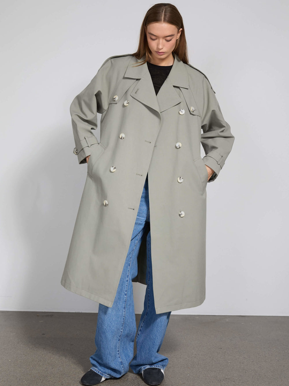 A model wears a stylish light gray trench coat with large buttons, paired with wide-leg jeans, showcasing MEOTINE's modern design.