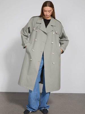 A model wears a stylish light gray trench coat with large buttons, paired with wide-leg jeans, showcasing MEOTINE's modern design.