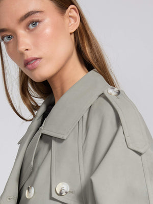 A close-up of a model wearing a light gray trench coat with a stylish collar and button details, showcasing MEOTINE's elegant design.
