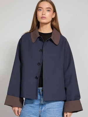A model wears a stylish navy blue MEOTINE jacket with a brown collar and cuffs, paired with light blue jeans.