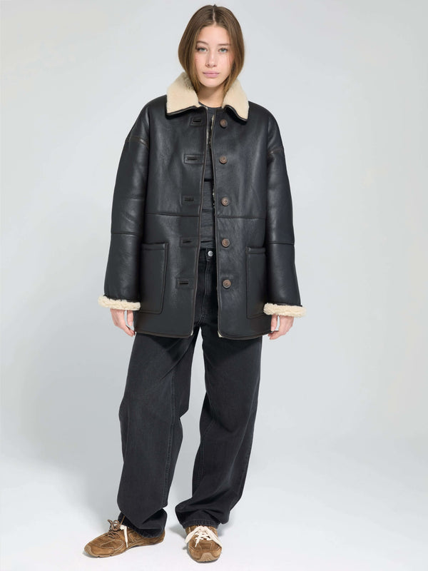 A model wears a stylish black leather jacket with a cozy cream collar, paired with dark jeans and casual shoes, showcasing MEOTINE's chic design.