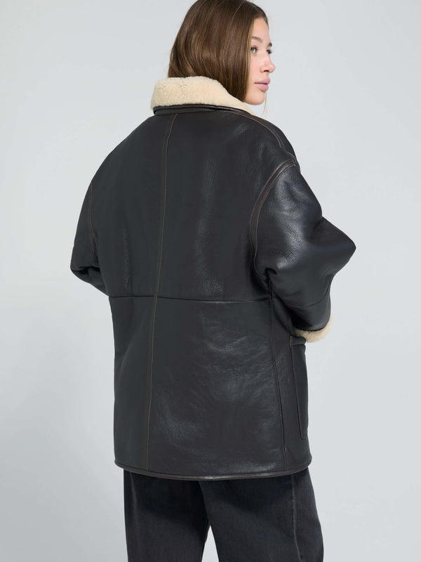 A model showcases a stylish black leather jacket with a cozy cream shearling collar, perfect for a chic winter look by MEOTINE.