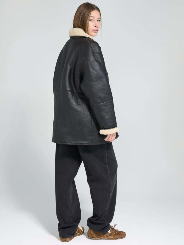A model wearing a black leather jacket with a shearling collar, paired with loose black pants, showcasing MEOTINE's stylish outerwear.