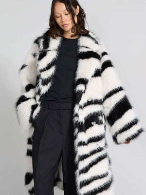 A model wears a stylish black and white striped faux fur coat by MEOTINE, paired with a simple black top and tailored pants.