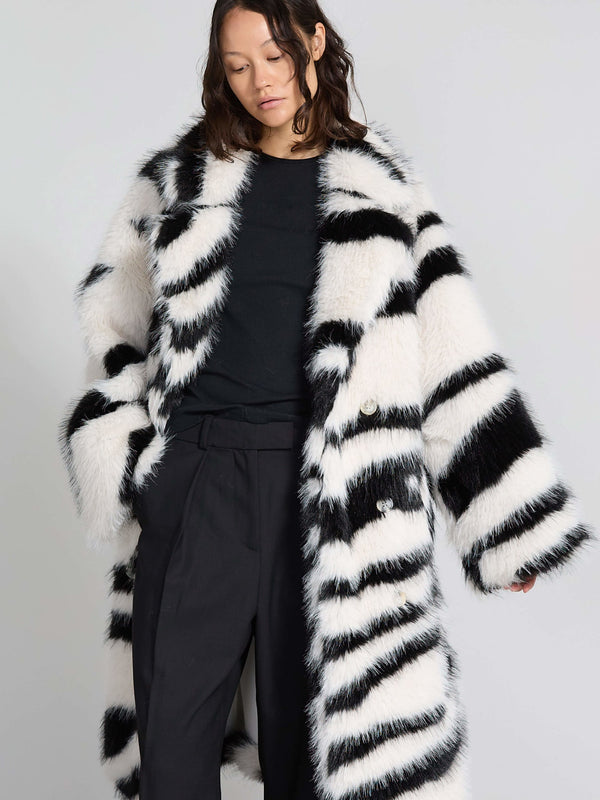 A model wears a stylish black and white striped faux fur coat by MEOTINE, paired with a simple black top and tailored pants.