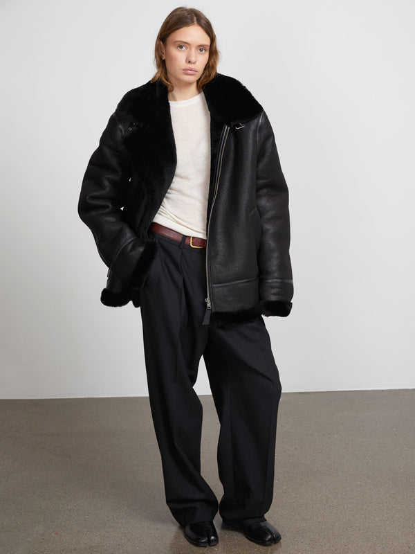 A model wears a black shearling jacket over a light top, paired with loose black trousers, showcasing MEOTINE's stylish outerwear.