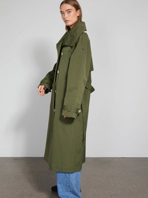 A model showcases a stylish olive green trench coat from MEOTINE, paired with blue jeans, set against a minimalist background.