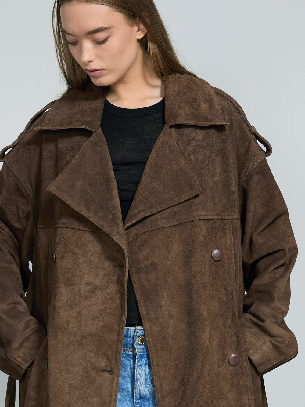 A model showcases a stylish brown suede trench coat by MEOTINE, paired with wide-leg jeans and a black top, set against a neutral backdrop.