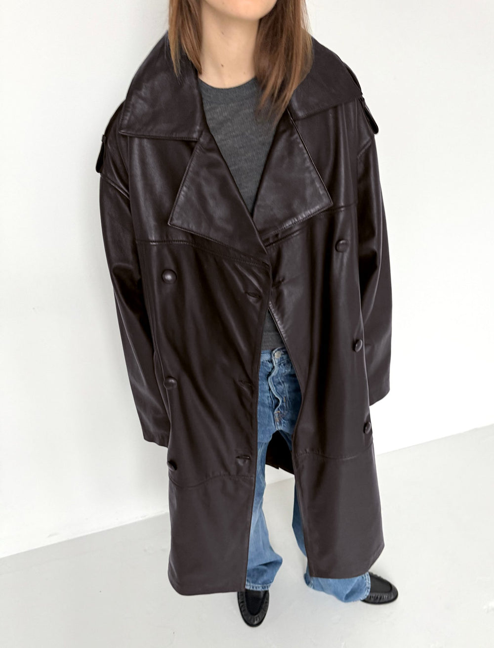 A model showcases a stylish brown leather trench coat paired with casual blue jeans, embodying modern fashion by MEOTINE.