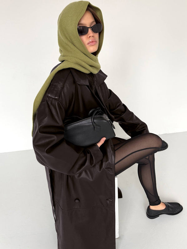 A model wearing a black oversized coat and green scarf, paired with sheer black tights and sunglasses, showcasing MEOTINE style.