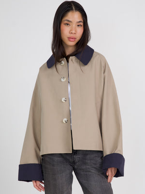 A model showcases a stylish beige jacket with a large collar and navy cuffs, featuring prominent buttons. MEOTINE's chic design stands out.