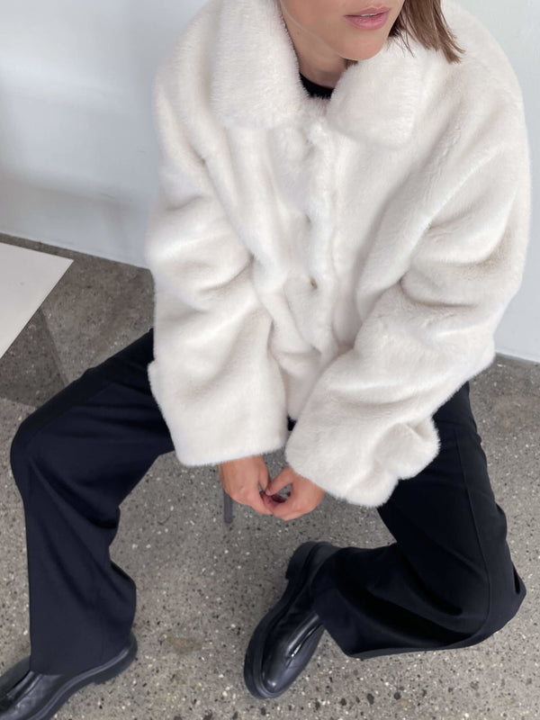 Cozy white faux fur jacket with a button-up front, paired with black pants, showcasing a stylish and comfortable look by MEOTINE.