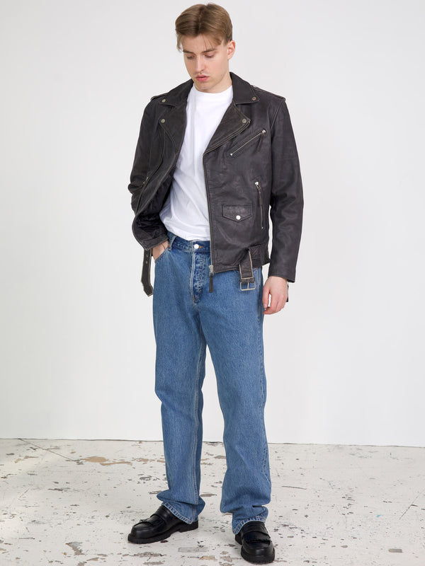 A model wearing a black leather biker jacket over a white t-shirt, paired with blue jeans and black shoes, showcasing MEOTINE style.