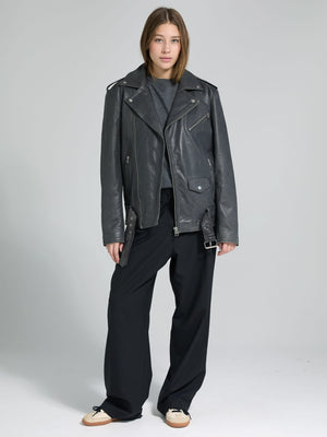 A model showcases a stylish black leather biker jacket paired with loose black trousers, embodying a chic, edgy look by MEOTINE.
