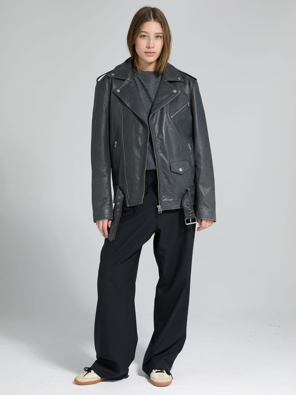 A model showcases a stylish black leather biker jacket paired with loose black trousers, embodying a chic, edgy look by MEOTINE.
