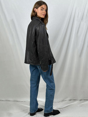A model showcases a stylish black leather jacket from MEOTINE, paired with blue jeans, against a neutral backdrop.