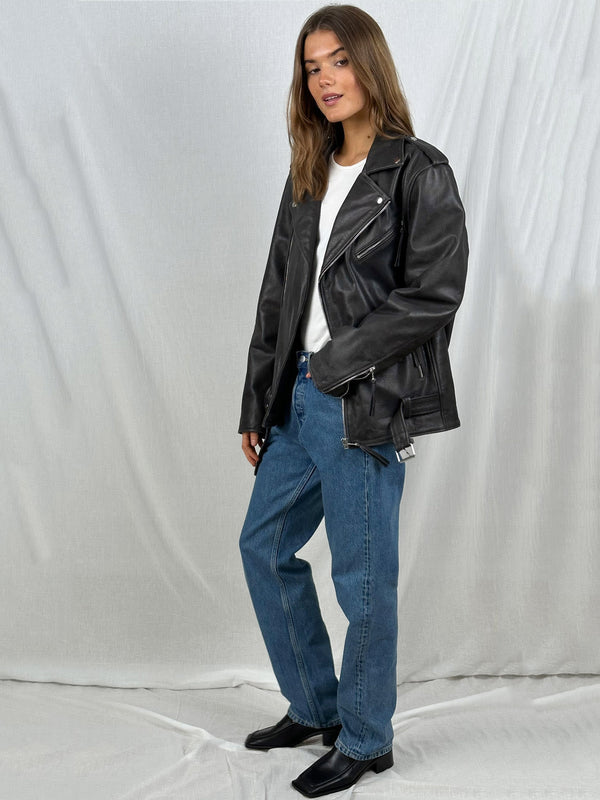 A model wearing a black leather biker jacket over a white t-shirt, paired with blue jeans and black boots, showcasing MEOTINE style.