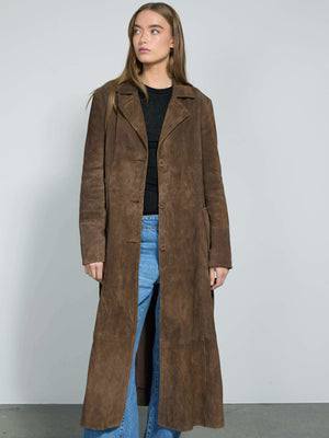 A model showcases a long brown suede coat by MEOTINE, paired with a black top and blue wide-leg jeans against a neutral backdrop.