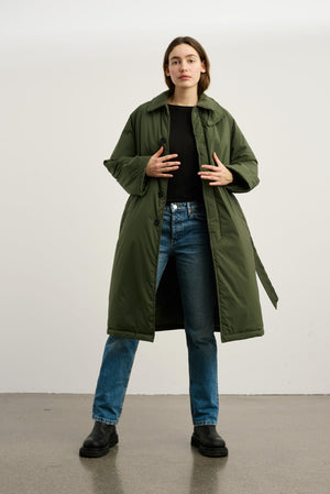 A model wearing a long olive green puffer coat over a black top and blue jeans, showcasing MEOTINE's stylish outerwear.