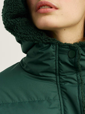 A close-up of a woman's face wearing a green MEOTINE jacket with a cozy, textured hood, highlighting her lips and skin.