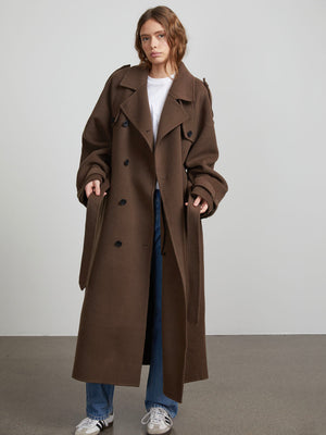 A model wears a stylish brown oversized trench coat by MEOTINE, paired with a white t-shirt and blue jeans, set against a neutral backdrop.