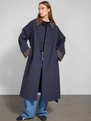 A model showcases a stylish navy coat with a contrasting brown collar, paired with wide-leg jeans, embodying MEOTINE's modern aesthetic.