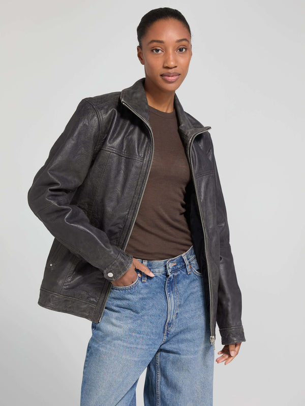 A model showcases a stylish black leather jacket from MEOTINE, paired with a brown top and light blue jeans against a neutral background.