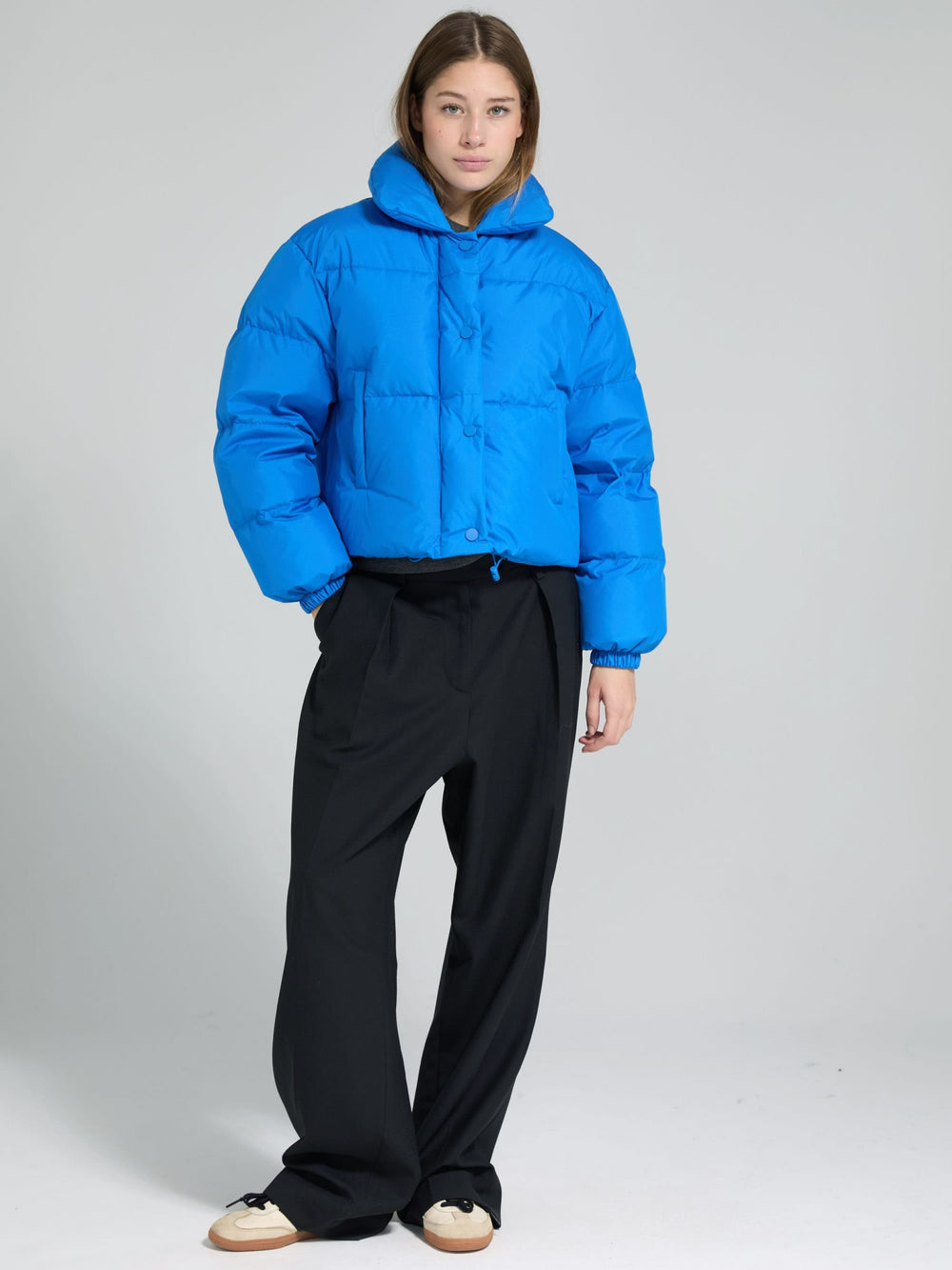 A model showcases a vibrant blue puffer jacket with a high collar and button closure, perfect for stylish warmth by MEOTINE.