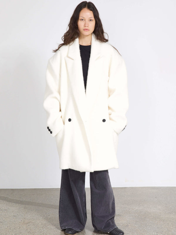 A model wears a cozy white oversized coat with black buttons, paired with dark wide-leg pants, showcasing MEOTINE's stylish design.