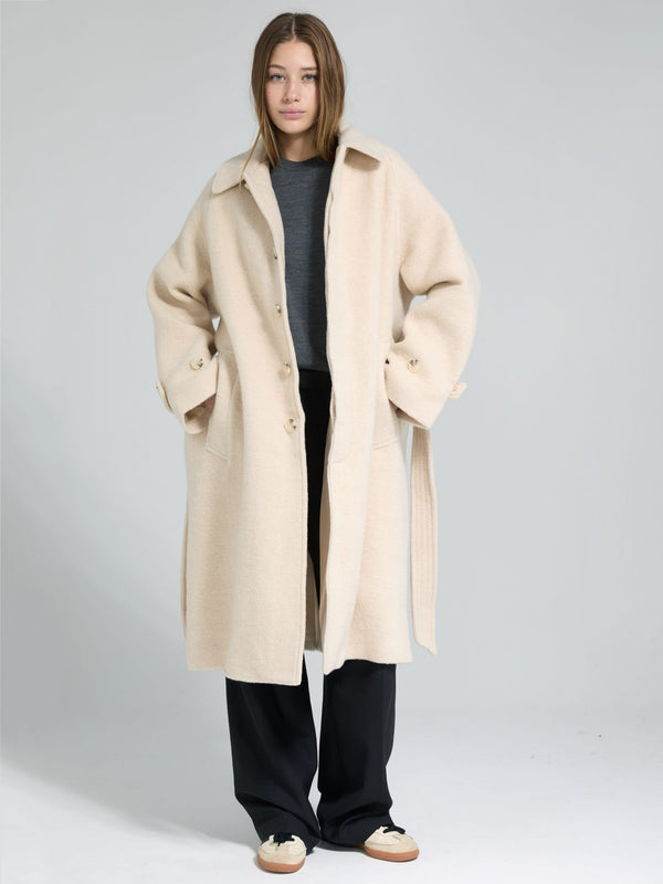 A model wears a cozy beige MEOTINE coat over a gray top, paired with black pants, showcasing a stylish and relaxed look.