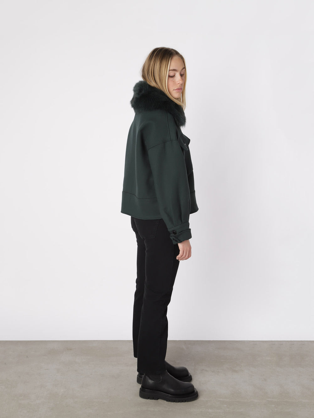 A model wearing a dark green cropped jacket with a faux fur collar, showcasing a stylish and modern look by MEOTINE.