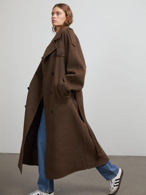 A model showcases a stylish brown oversized trench coat by MEOTINE, paired with blue jeans and white sneakers, exuding elegance.