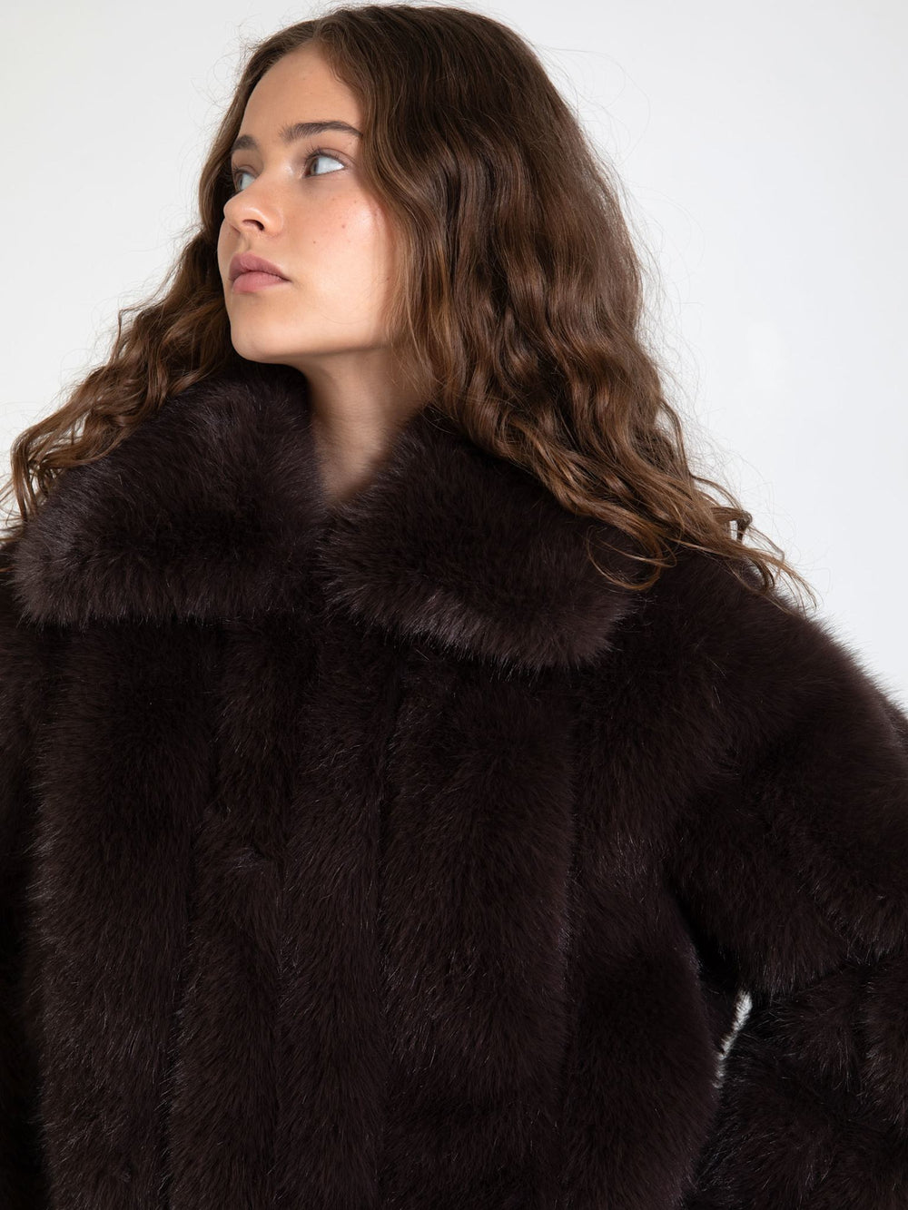A model wears a luxurious dark brown fur coat with a high collar, paired with casual blue jeans, showcasing MEOTINE's elegant style.