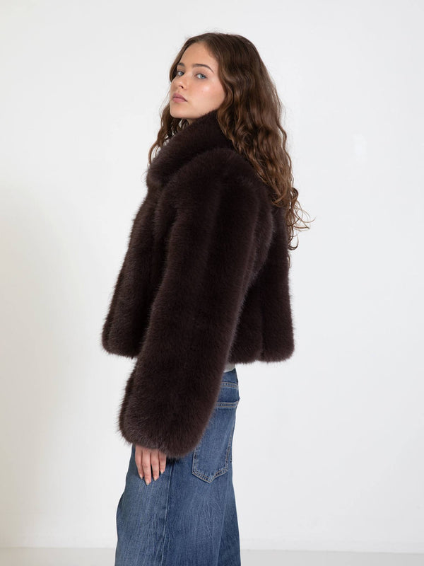 A model showcases a luxurious dark brown faux fur jacket by MEOTINE, styled with wide-leg jeans against a minimalist backdrop.
