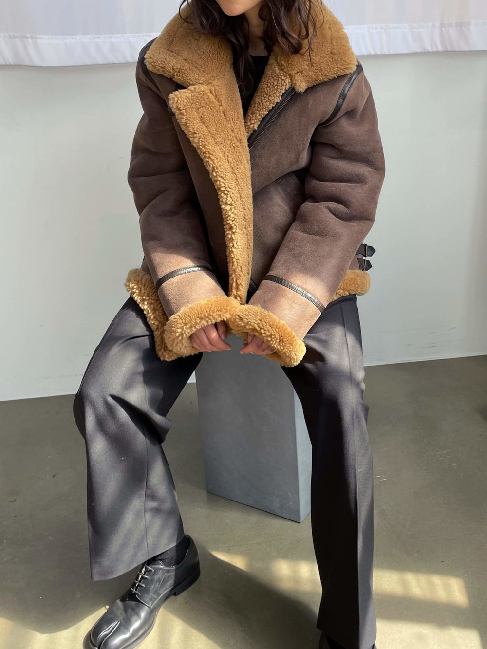 A model wears a stylish brown shearling jacket with a cozy tan collar and cuffs, showcasing MEOTINE's chic design.