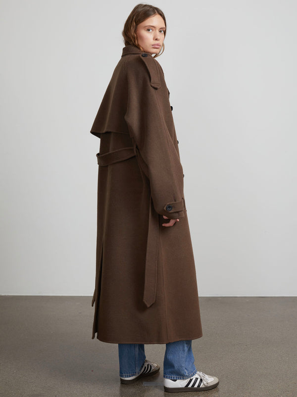 A model showcases a stylish brown trench coat with a cape design, paired with casual jeans and sneakers, by MEOTINE.