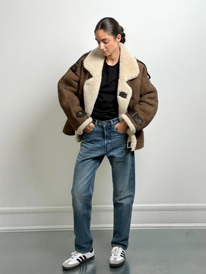 A model wearing a brown shearling jacket with a cozy collar, paired with blue jeans and sneakers, showcasing MEOTINE's stylish outerwear.