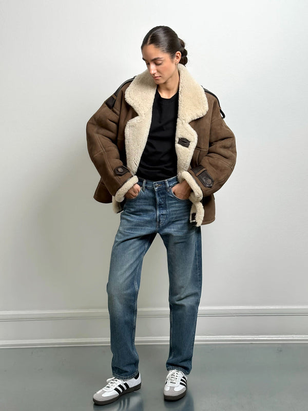A model wearing a brown shearling jacket with a cozy collar, paired with blue jeans and sneakers, showcasing MEOTINE's stylish outerwear.
