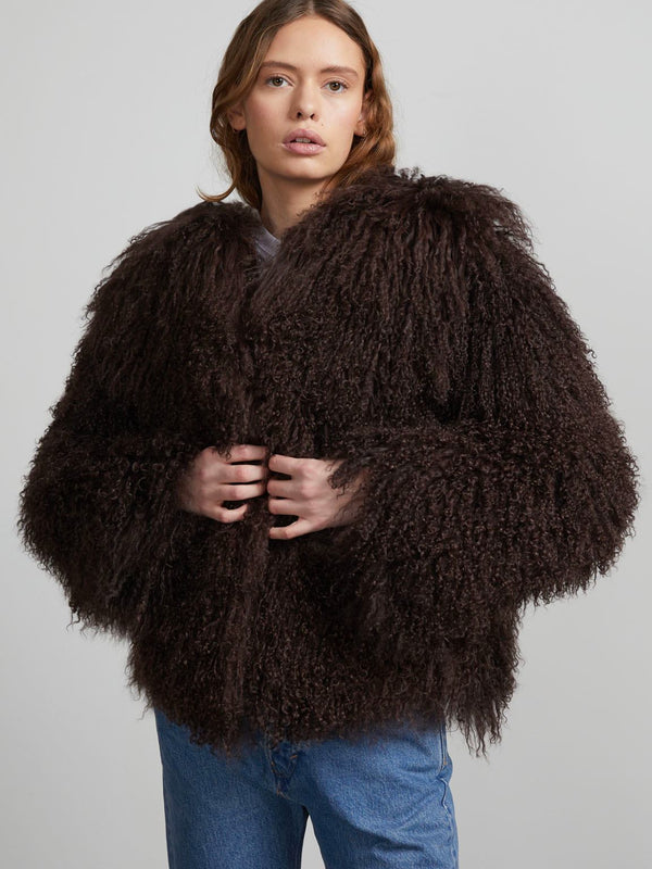 A model wears a fluffy, dark brown MEOTINE jacket with a voluminous silhouette, styled with casual blue jeans.