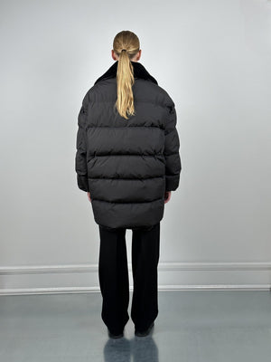 A model wearing a black oversized puffer jacket from MEOTINE, viewed from the back, paired with black wide-leg pants.