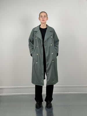 A model stands confidently in a stylish, oversized green trench coat by MEOTINE, paired with black pants and shoes.