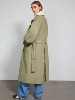 A model wearing a long olive green coat with a fur collar, styled with loose blue jeans, showcasing MEOTINE's chic design.