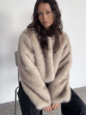 A model sits in a chair wearing a soft, oversized beige sweater with long sleeves, showcasing the cozy style of MEOTINE.