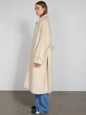 A model showcases a cream-colored, oversized coat with a belt, paired with blue jeans, representing MEOTINE's stylish design.